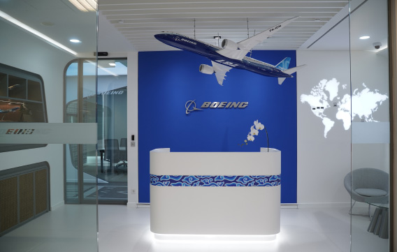 A modern office reception area featuring a Boeing logo and a model 787-10 airplane suspended from the ceiling.
