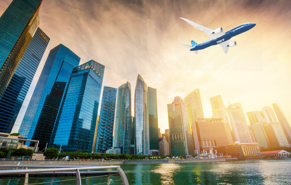 A Boeing 787-9 flying over the SIngapore skyline with a glowing sun in the background.