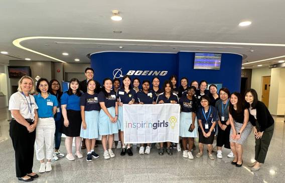 A diverse group of individuals posing with an "Inspiring Girls" banner at a Boeing office.